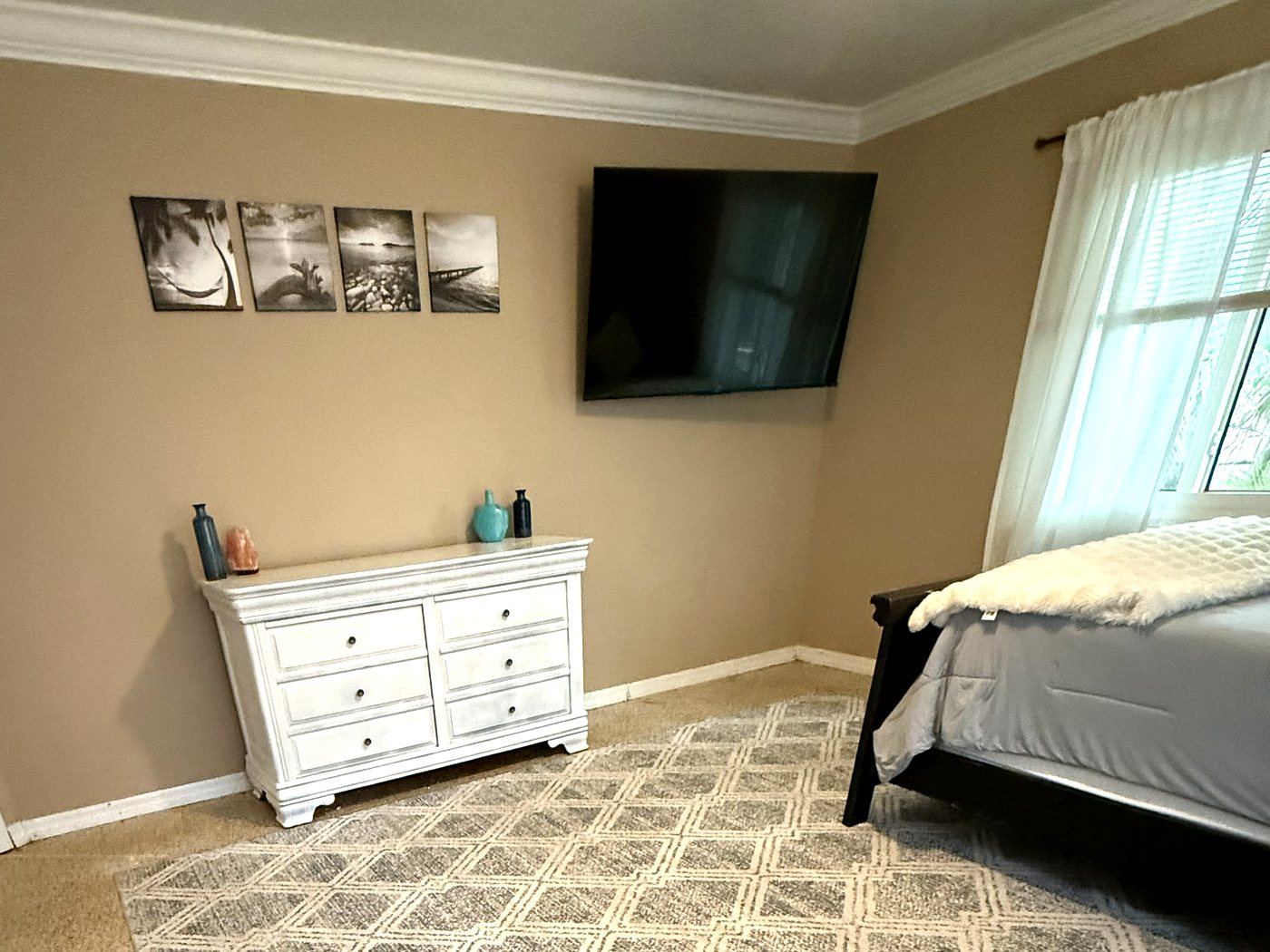 Refinished white dresser below a mounted TV and framed prints
